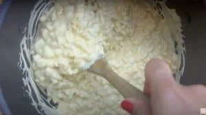 Creamy mac and cheese being stirred in a pot with a wooden spoon.